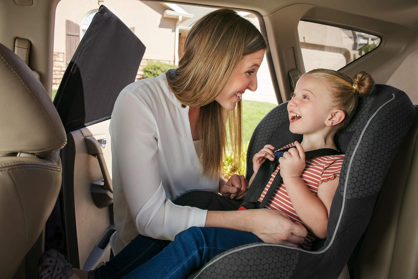 Woman adjusting a child's car seat in a vehicle, side window is covered with a sun shade