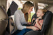Woman adjusting a child's car seat in a vehicle, side window is covered with a sun shade