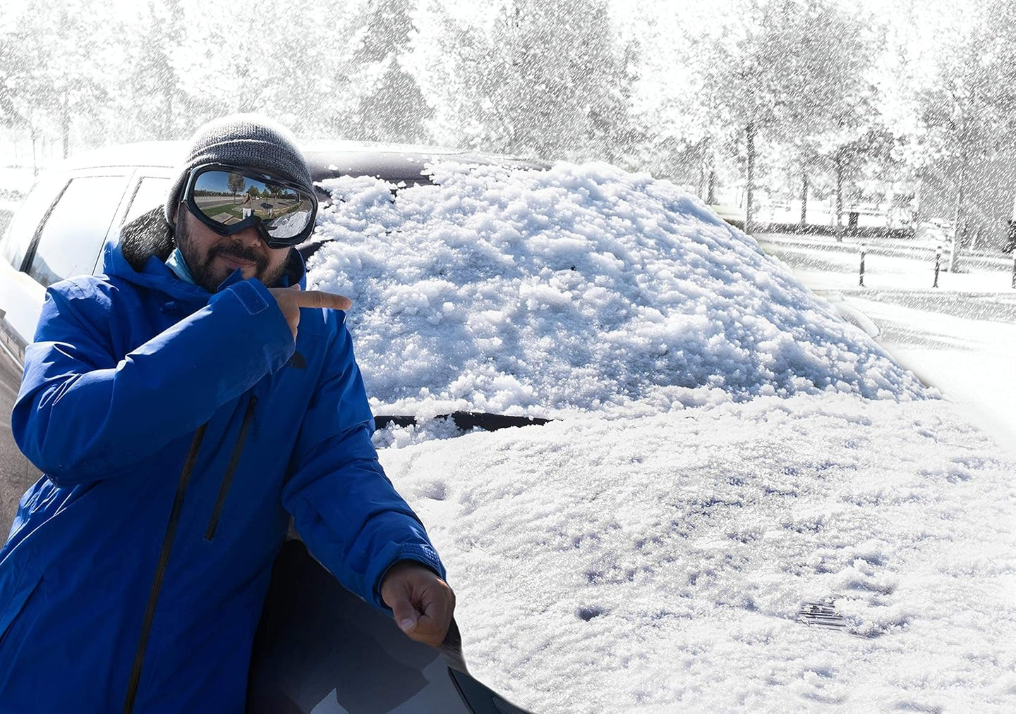 Person in a blue coat sitting next to a snow-covered car in a snowy landscape.