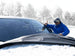 Person in blue jacket and goggles standing next to a car with snow cover on the car